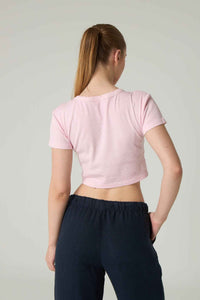 Person wearing a pink crop top and navy pants on a plain background.