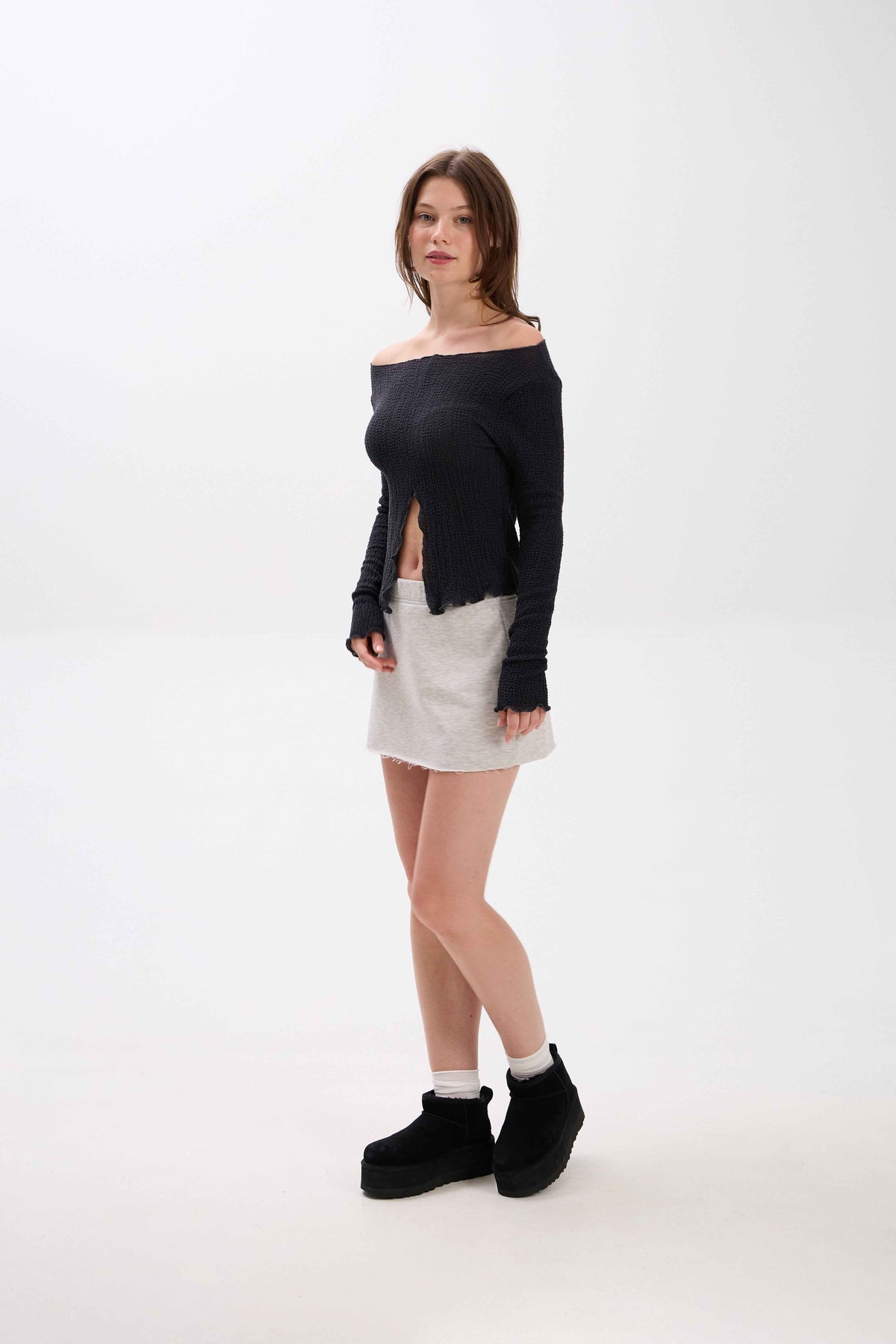 Person wearing a black off-shoulder top, white skirt, and black platform boots on a white background.