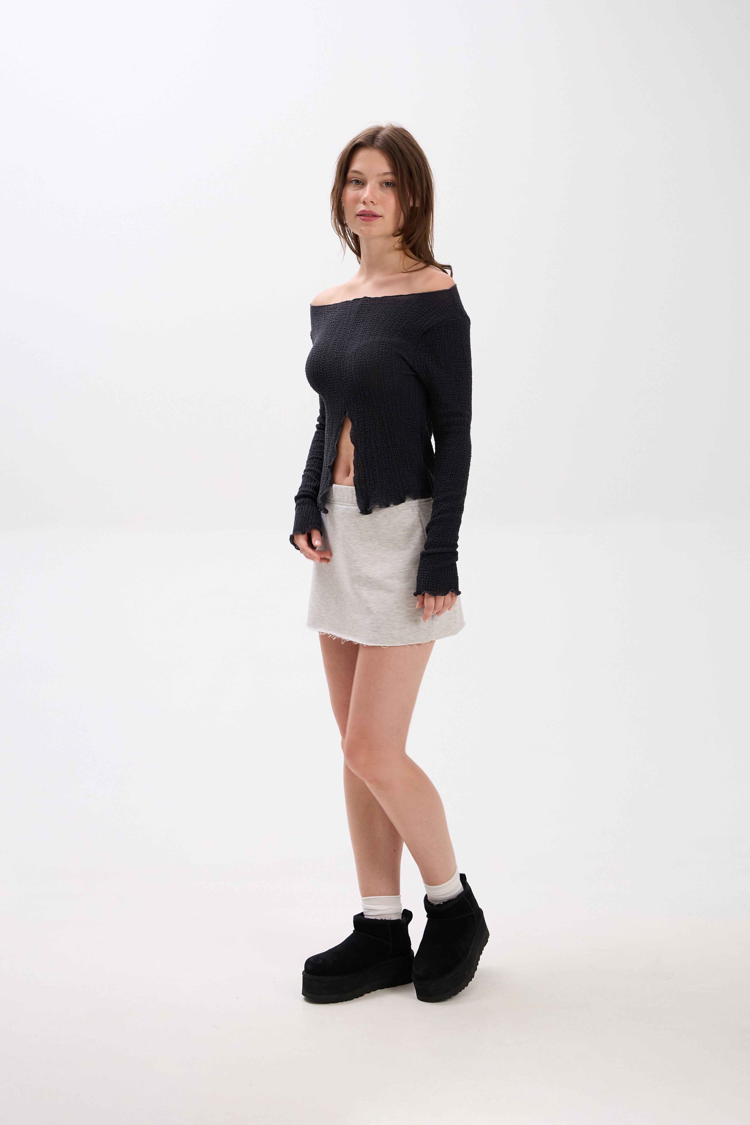 Person wearing a black off-shoulder top, white skirt, and black platform boots on a white background.