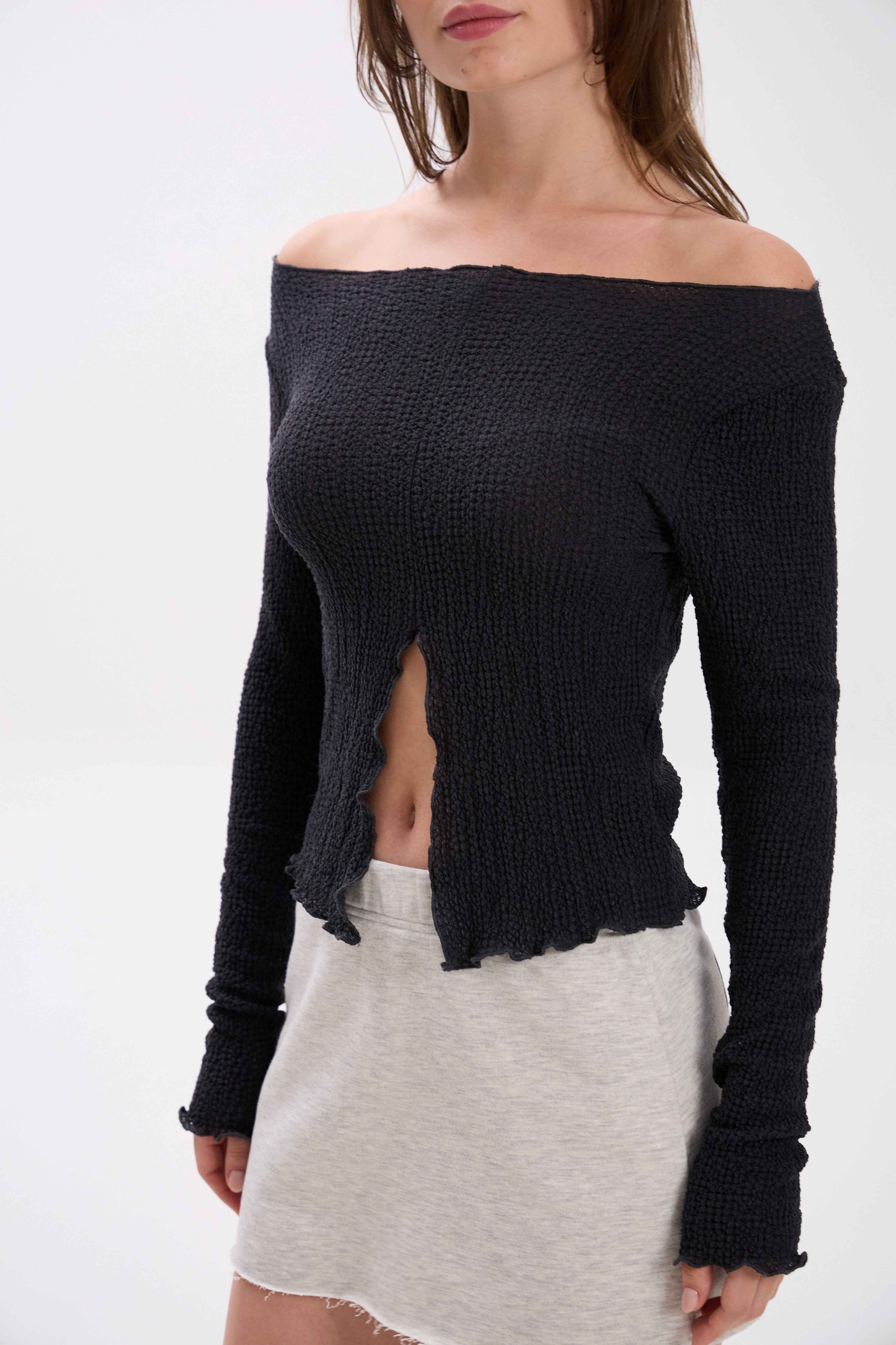 Woman wearing a black off-shoulder top and white skirt on a white background.