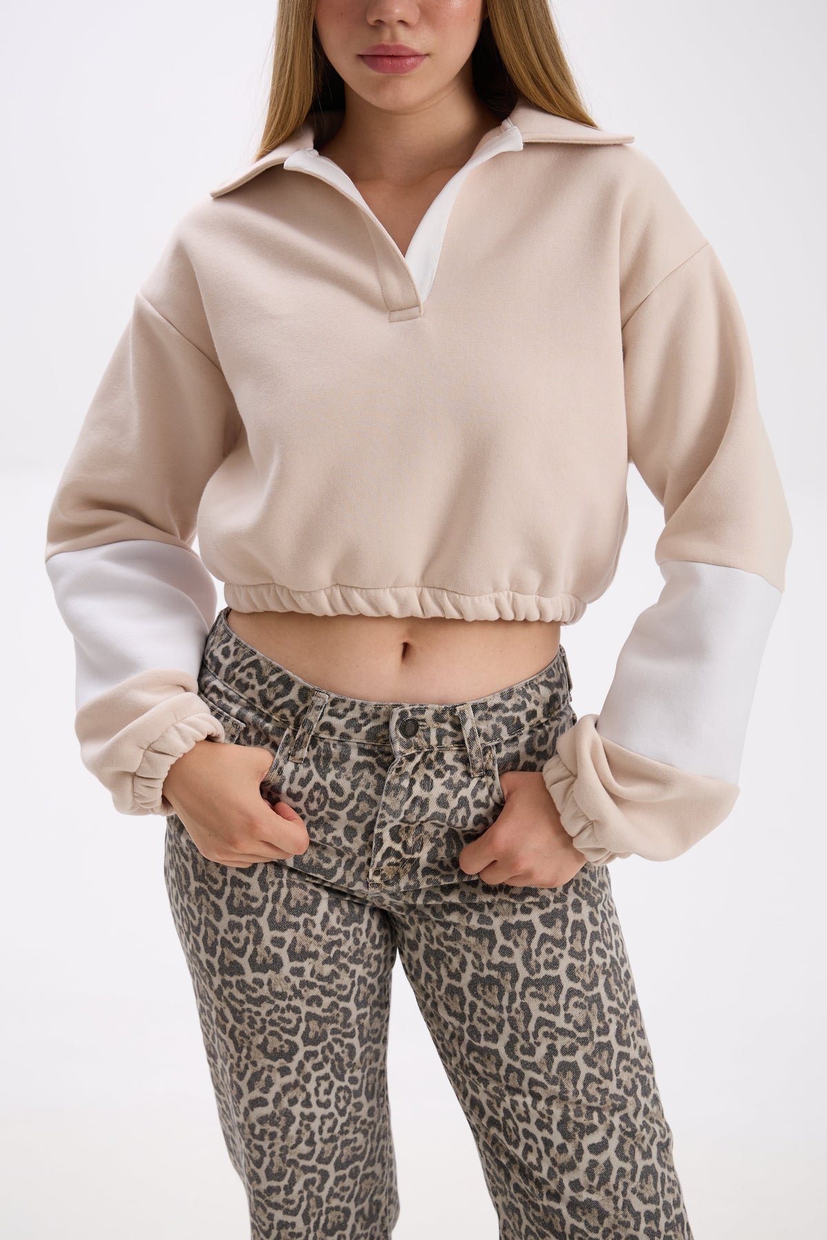 Person wearing a beige and white cropped sweatshirt with leopard print pants on a white background.