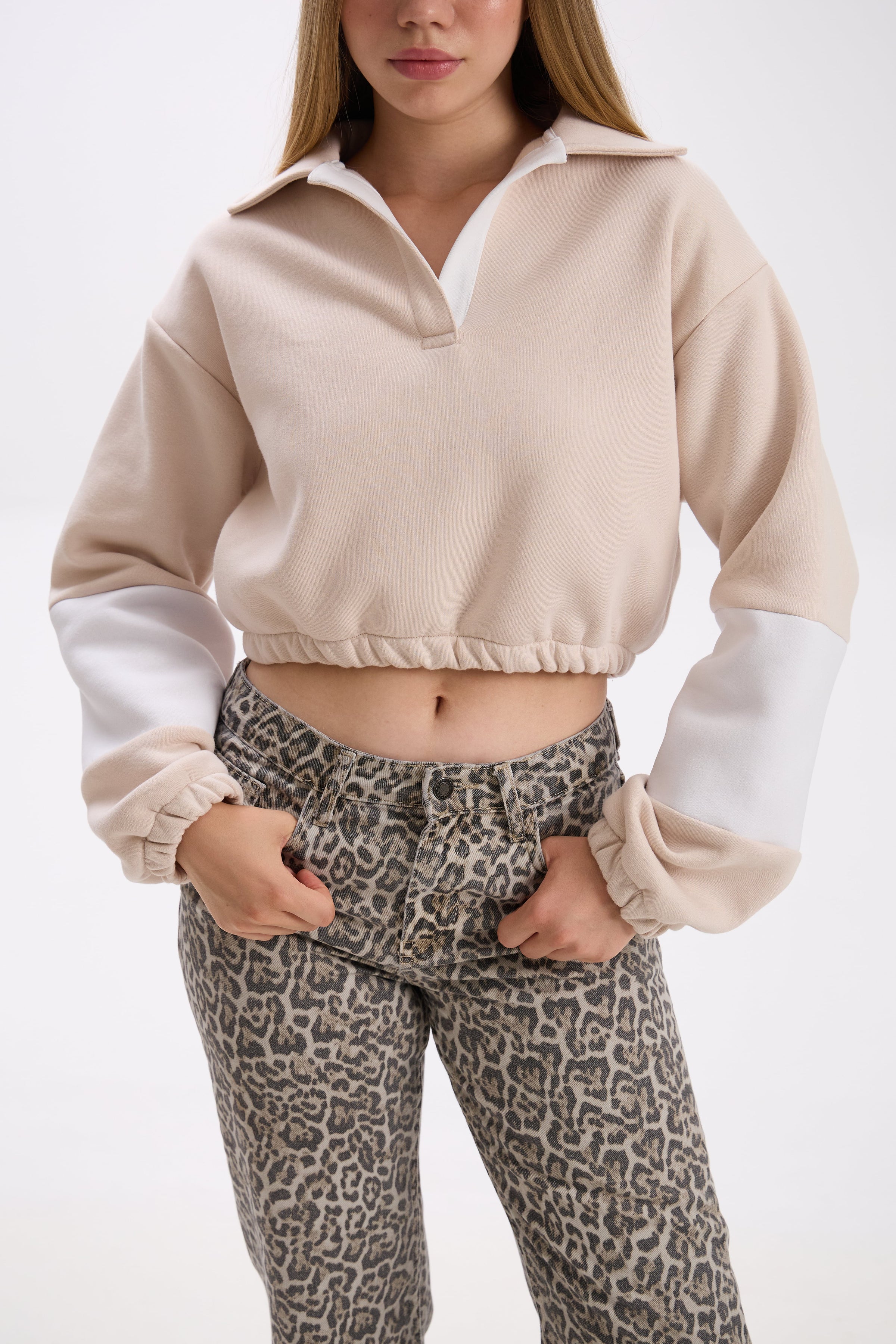 Person wearing a beige and white cropped sweatshirt with leopard print pants on a white background.