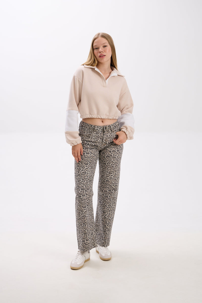 Woman wearing a beige cropped jacket and patterned pants on a white background.