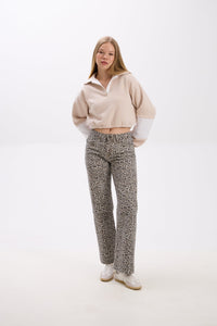 Person wearing a beige sweater and patterned pants on a white background.