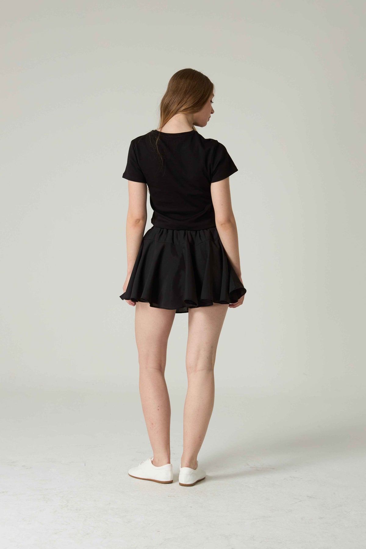 Person wearing a black t-shirt and skirt on a plain background.