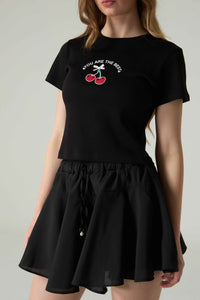 Person wearing a black t-shirt with a cherry graphic and "YOU ARE THE BEST" text, paired with black shorts on a plain background.