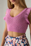 Woman wearing a pink knitted crop top with floral pants against a neutral background.