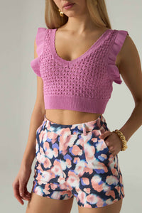 Woman wearing a pink crochet top and floral shorts against a neutral background.