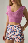 Woman wearing a pink crochet top and floral shorts against a neutral background.