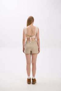 Person wearing a beige romper with a tie detail on a white background.