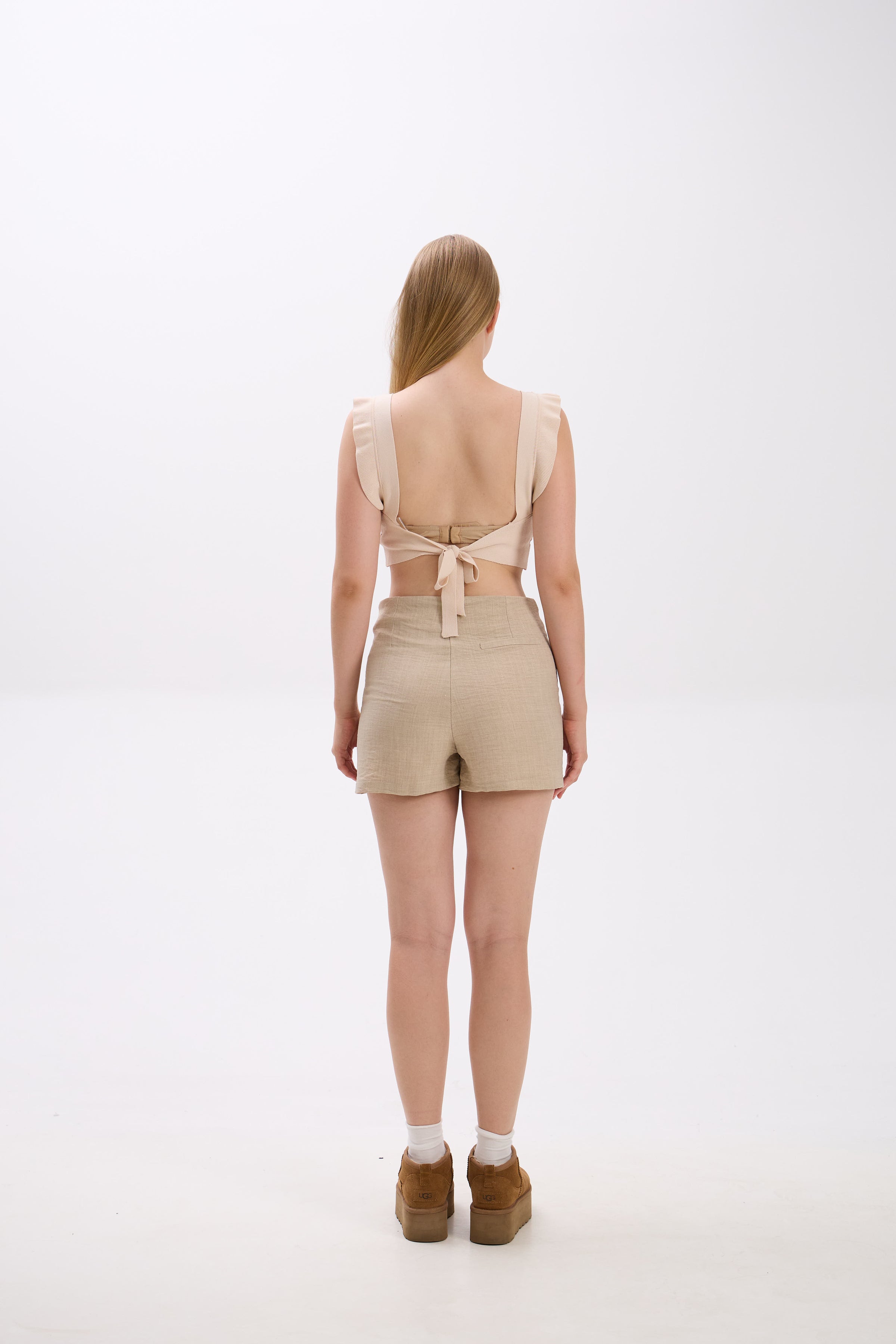 Person wearing a beige romper with a tie detail on a white background.