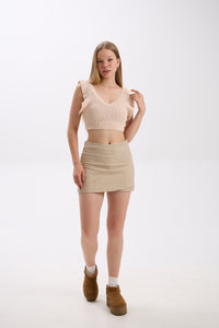 Woman wearing a beige crop top and skirt with brown shoes on a white background.