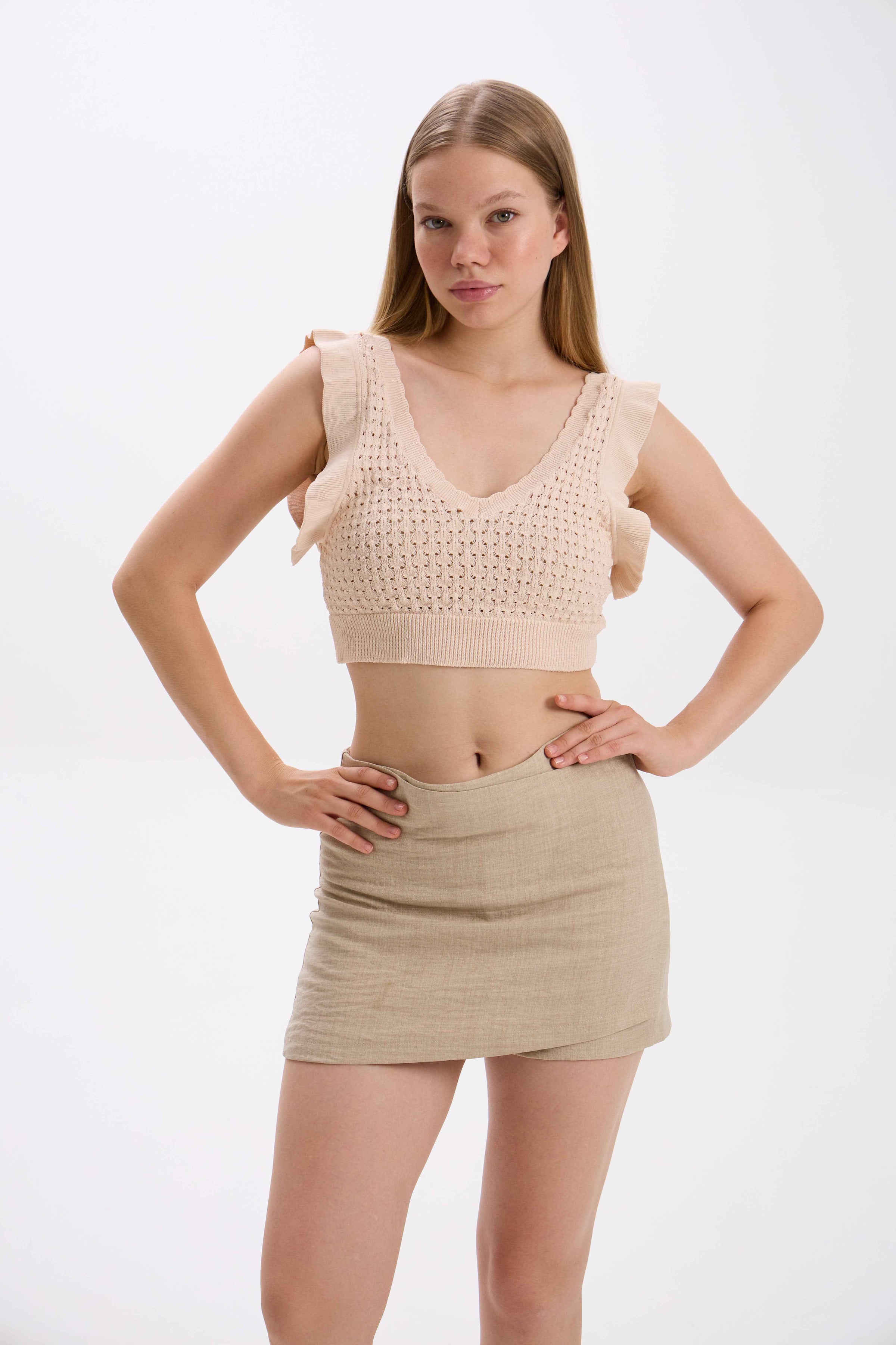 Woman wearing a beige crochet top and skirt on a white background.