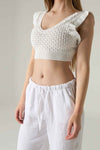 Person wearing a white knit crop top and white pants on a plain background.