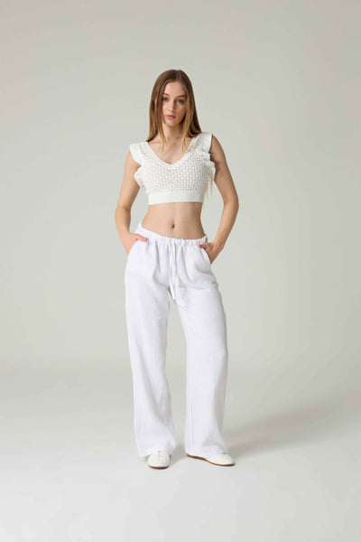 Woman wearing a white crochet top and wide-leg pants on a plain background.