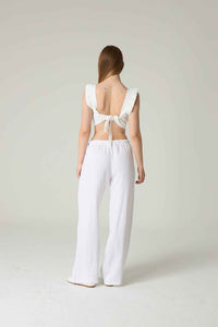 Woman wearing a white outfit with a bow detail on a plain background.