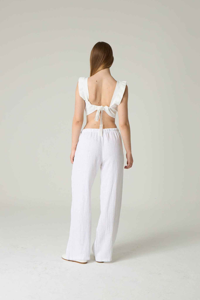 Woman wearing a white outfit with a bow detail on a plain background.