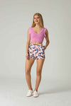 Woman wearing a pink crochet top and floral shorts on a plain background.