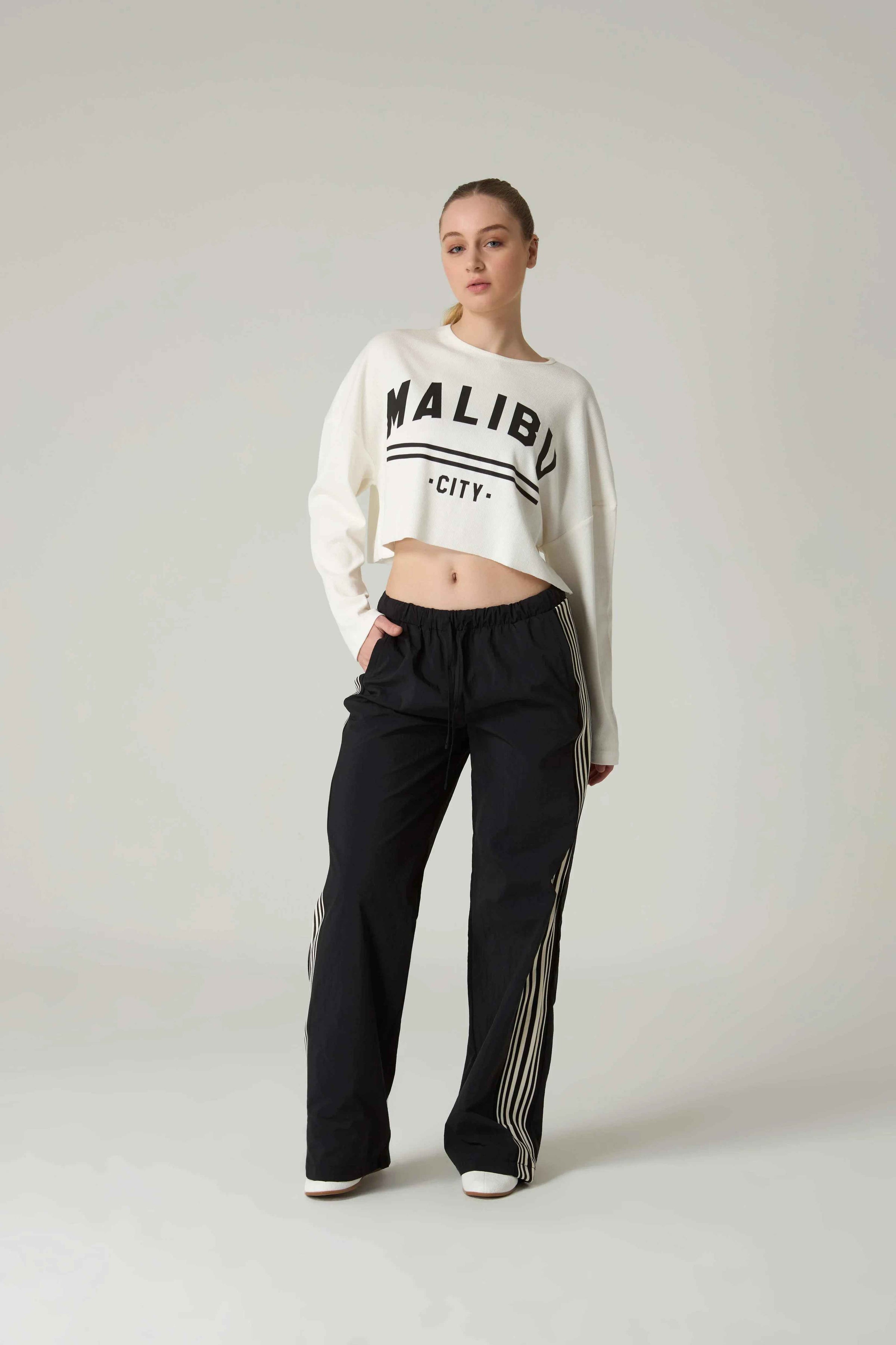 Person wearing a white sweatshirt with 'MALIBU CITY' embroidery and black pants on a plain background.