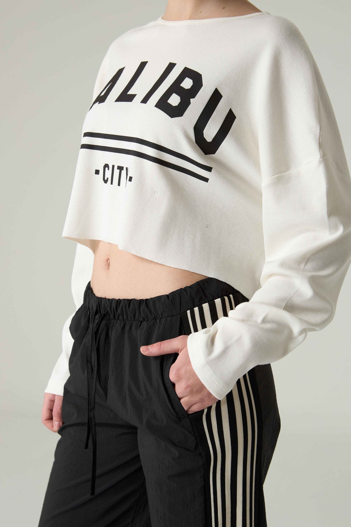 Person wearing a white cropped sweatshirt with 'MALIBU CITY' embroidery and black pants with stripes.
