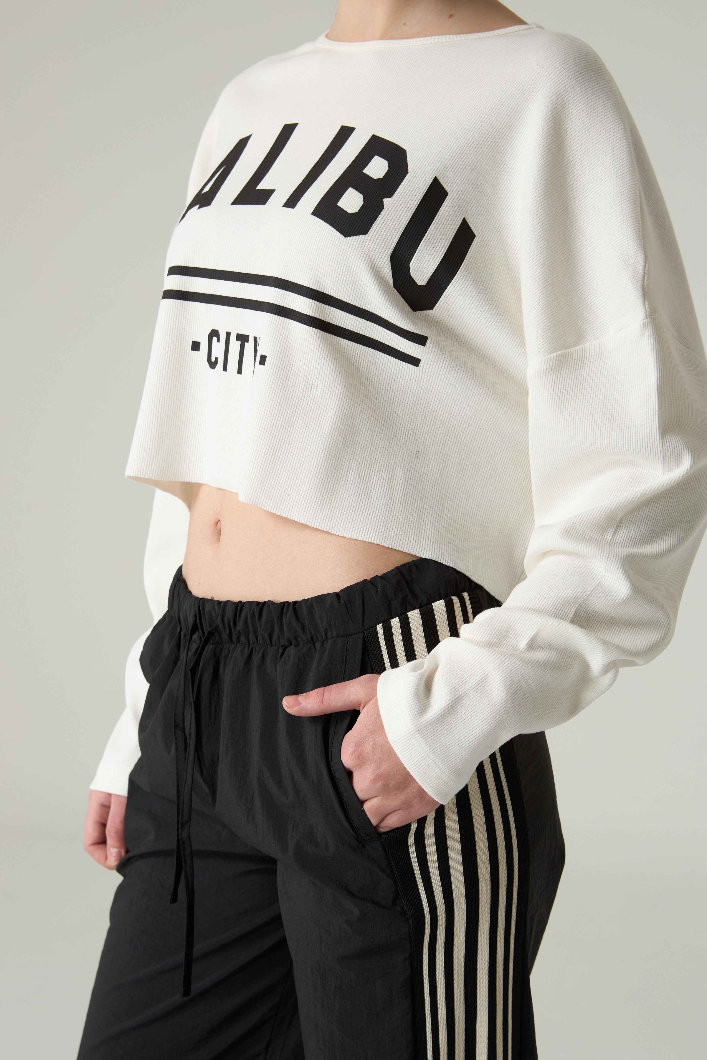 Person wearing a white cropped sweatshirt with 'MALIBU CITY' embroidery and black pants with stripes.