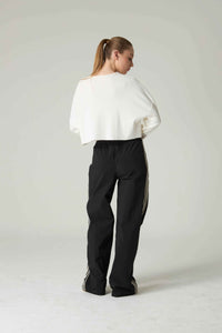 Person wearing a white top and black pants with white stripes on a light gray background.