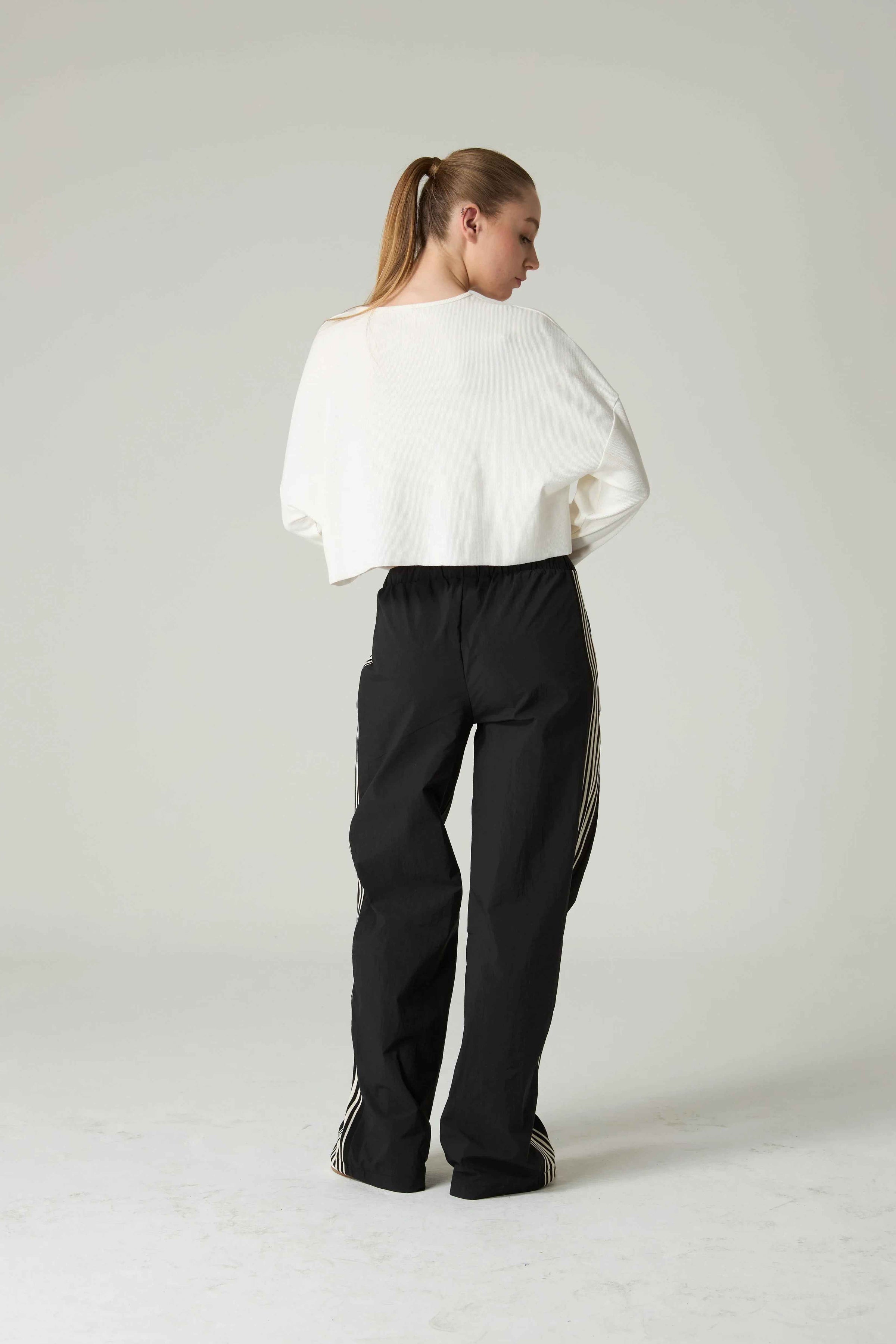 Person wearing a white top and black pants with white stripes on a light gray background.