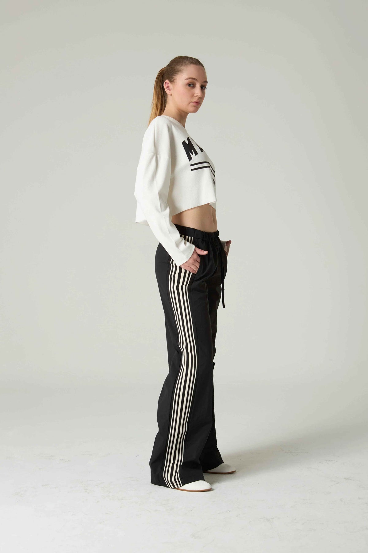 Person wearing a white cropped sweater and black pants with white stripes on a plain background.
