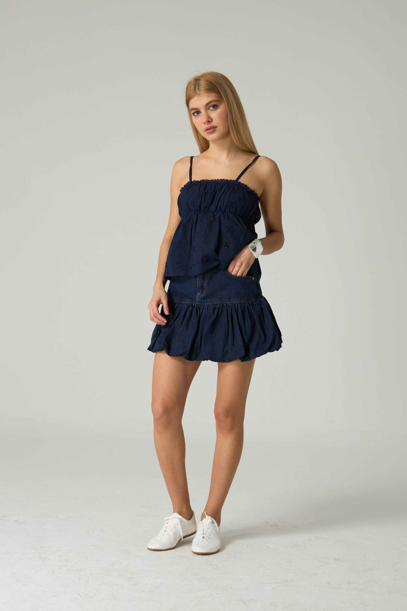 Woman wearing a navy blue dress with thin straps on a light gray background.