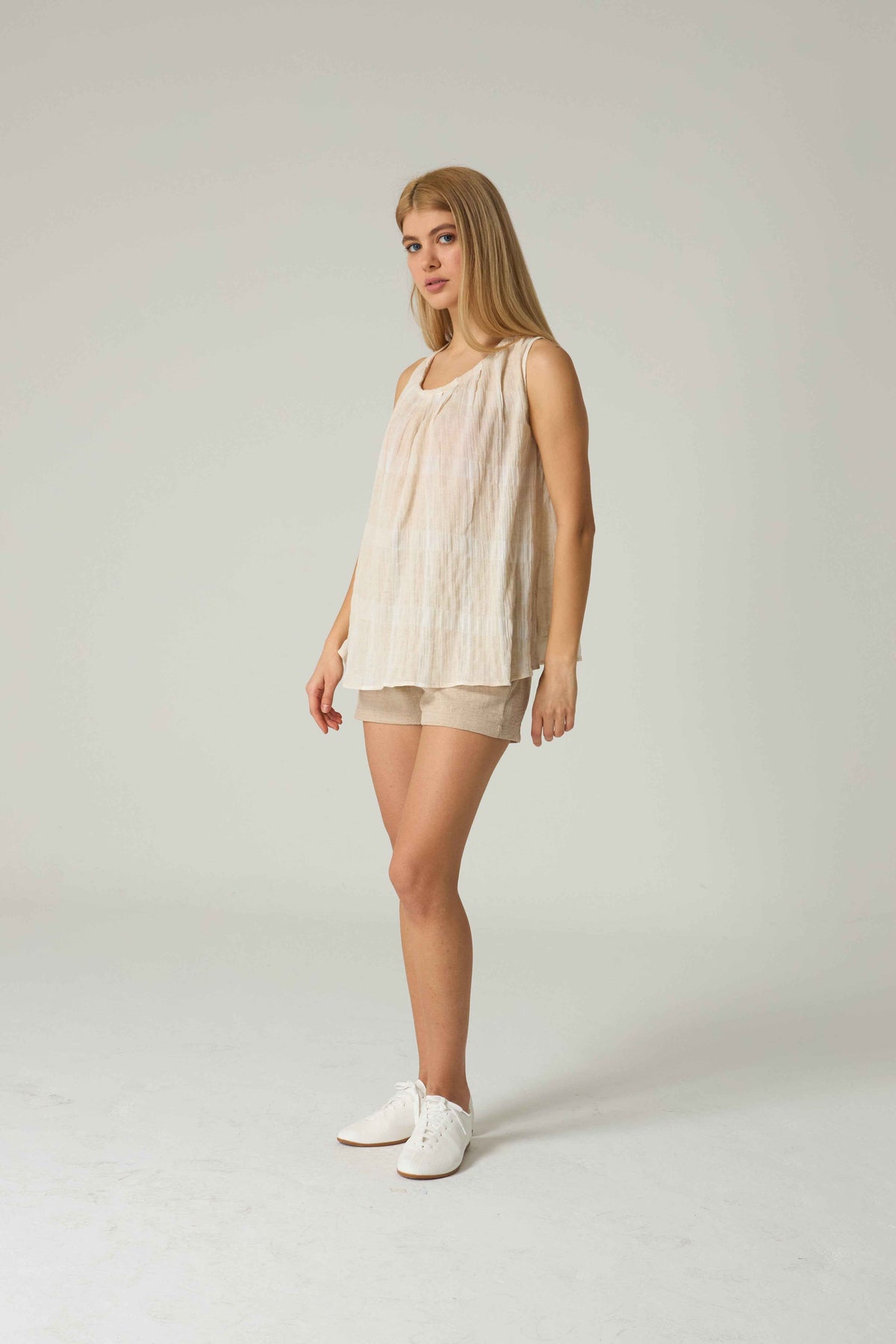 Woman wearing a beige sleeveless top and shorts on a white background.