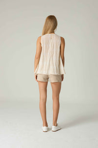 Woman wearing a beige sleeveless top and shorts on a plain background.