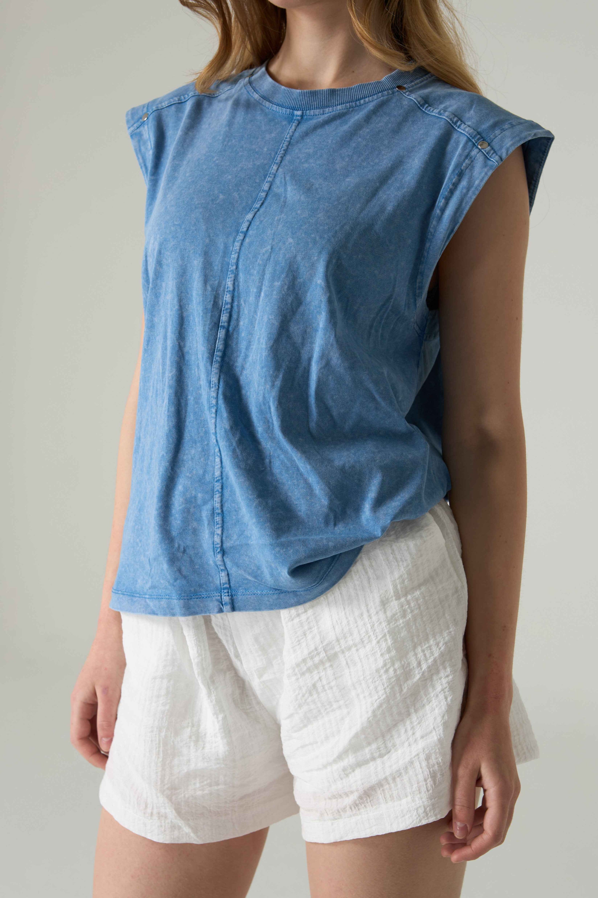 Person wearing a blue sleeveless top and white shorts against a neutral background.