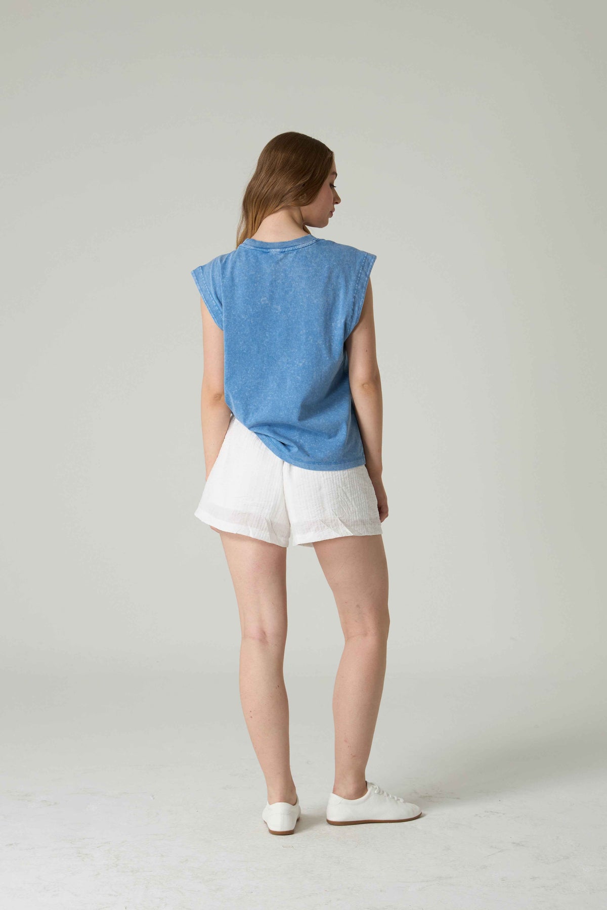 Woman wearing a blue top and white shorts on a plain background.