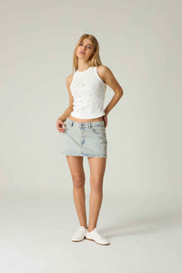 Woman wearing a white sleeveless top and light blue denim skirt on a plain background.