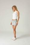 Woman wearing a white sleeveless top and denim skirt on a plain background.