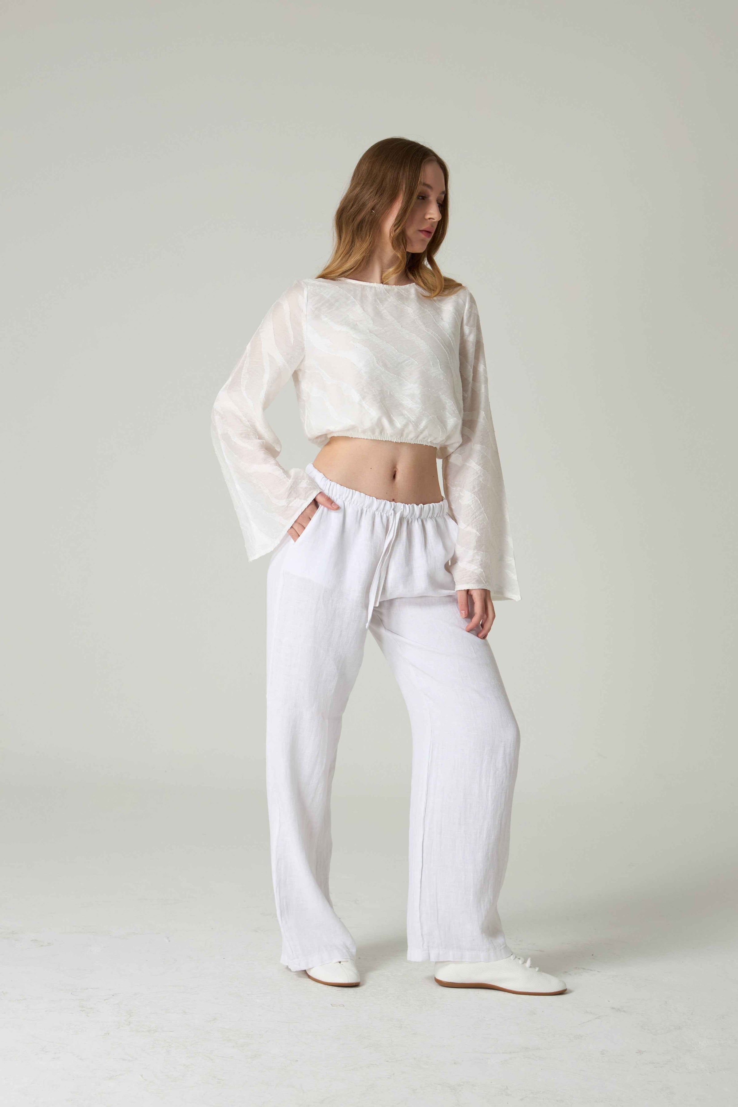 Woman wearing a white outfit with sheer sleeves on a plain background.