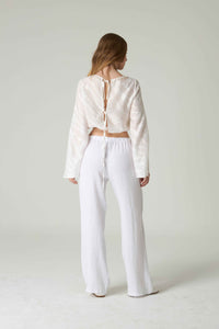 Person wearing a white lace-up top and white pants on a plain background.