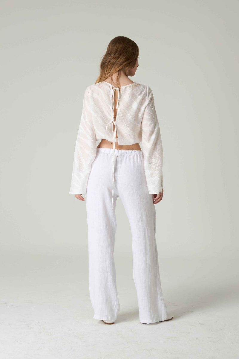 Person wearing a white lace-up top and white pants on a plain background.