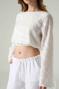 Person wearing a white textured top and white pants against a plain background.