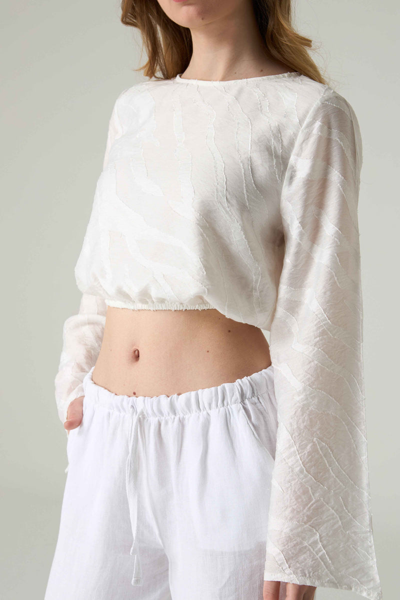 Person wearing a white textured top and white pants against a plain background.