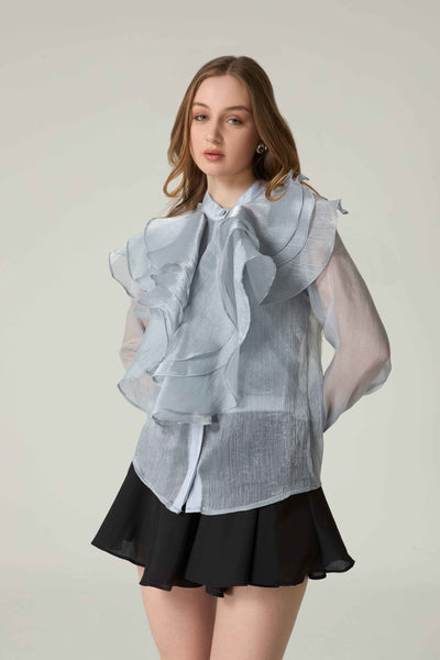 Woman wearing a light blue ruffled blouse and black skirt on a plain background.