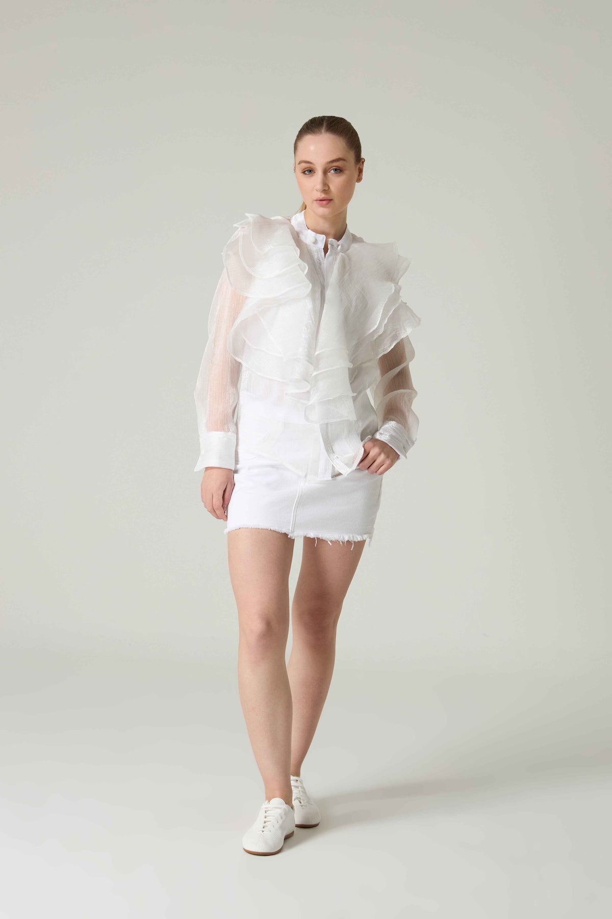 Person wearing a white outfit with sheer overlay on a plain background.
