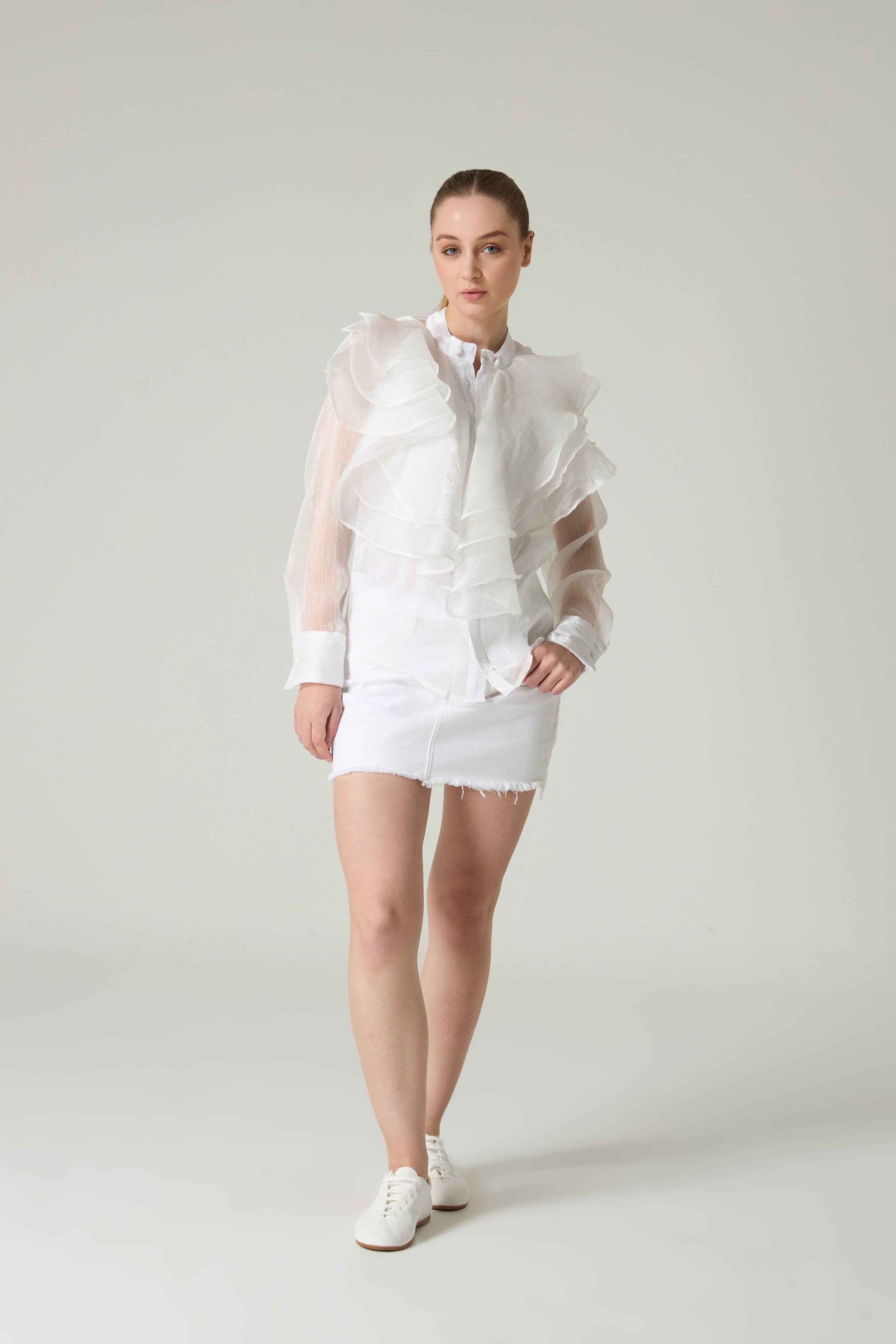 Person wearing a white outfit with sheer overlay on a plain background.