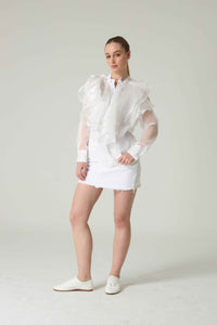 Woman wearing a white outfit with sheer sleeves against a plain background.