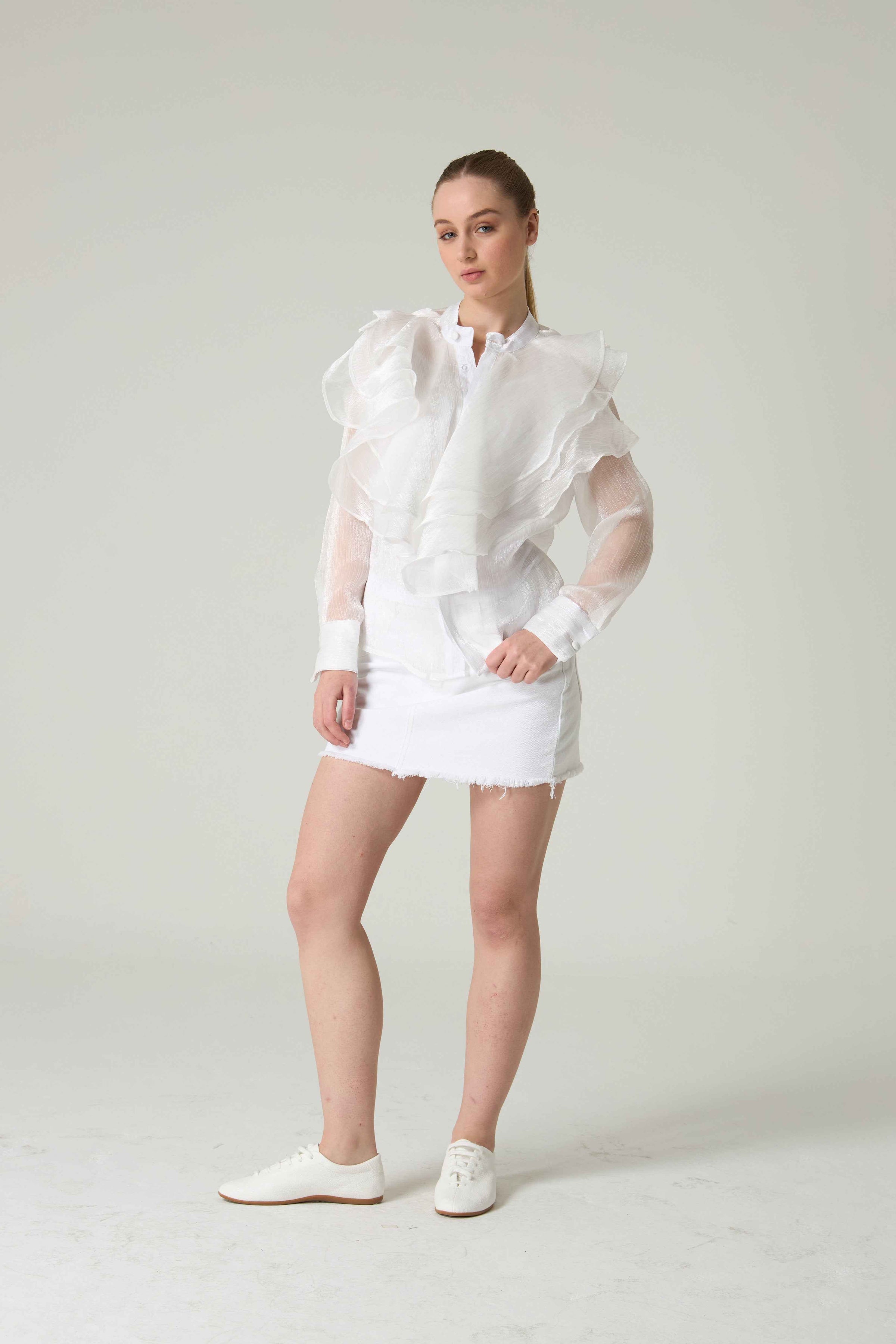 Woman wearing a white outfit with sheer sleeves against a plain background.