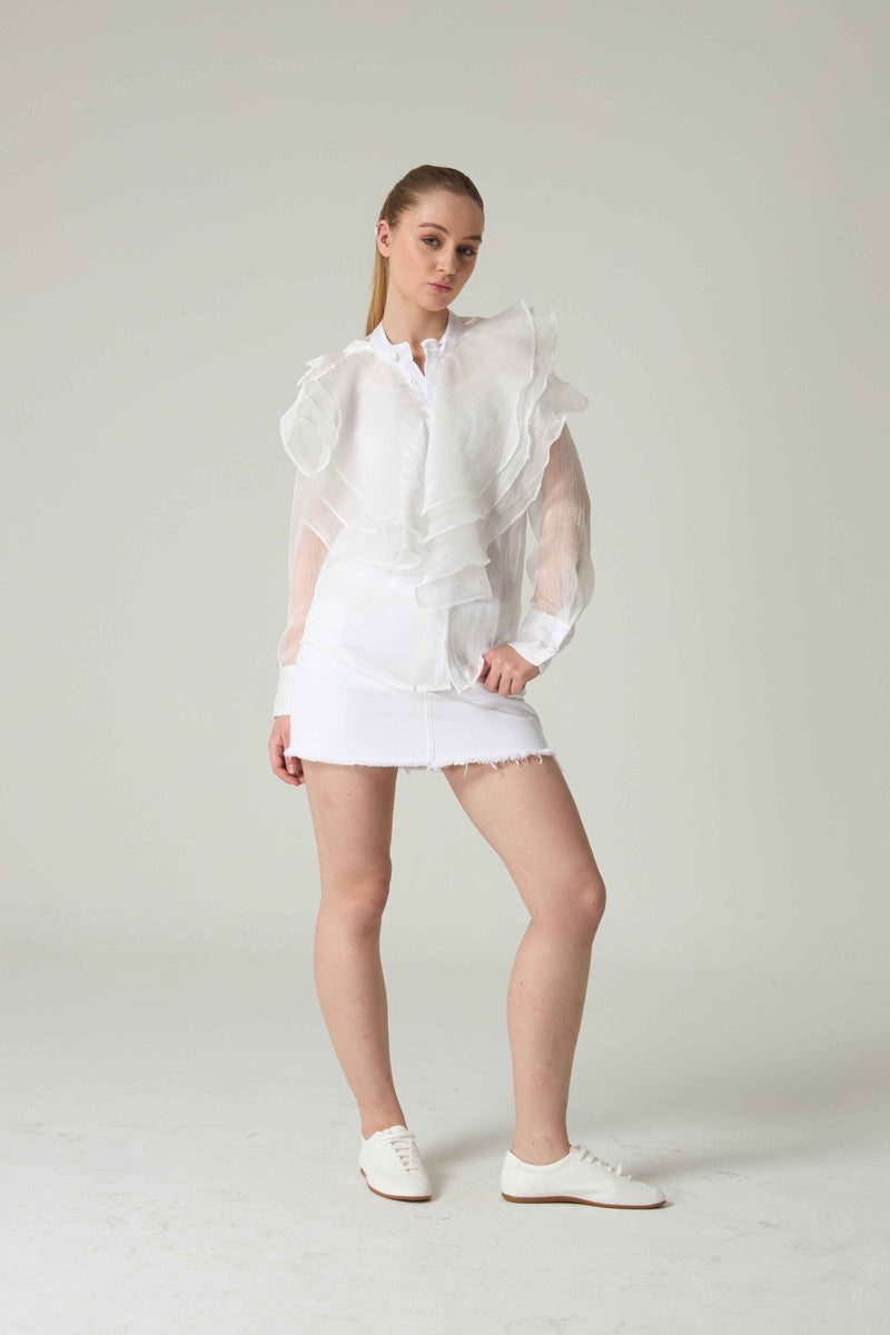 Woman wearing a white outfit with sheer sleeves against a plain background.