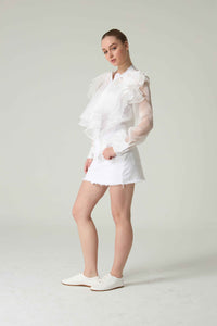 Woman wearing a white outfit with ruffled sleeves against a plain background.