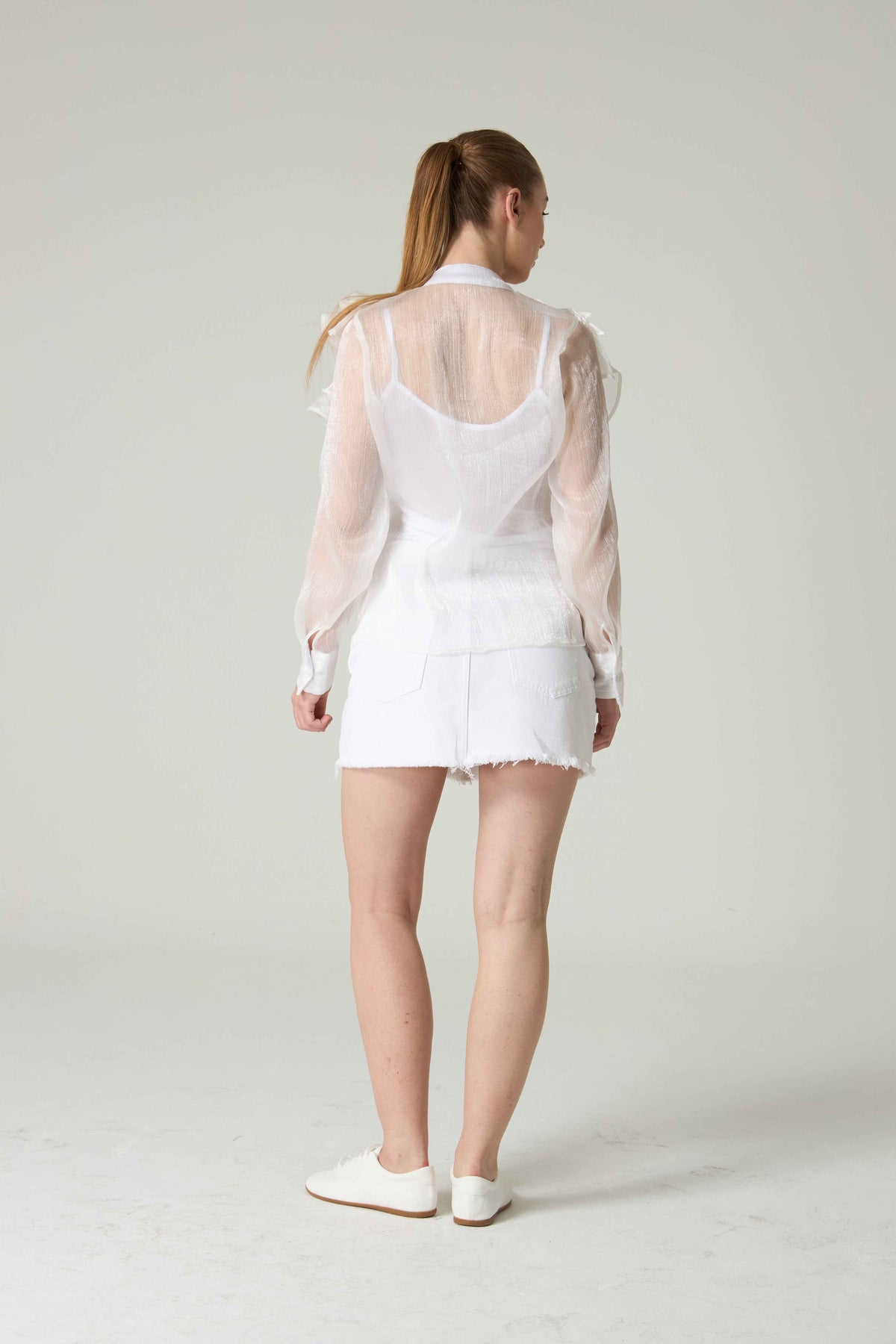 Person wearing a white outfit with sheer sleeves on a plain background.