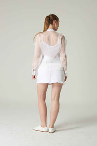 Person wearing a white outfit with sheer sleeves on a plain background.