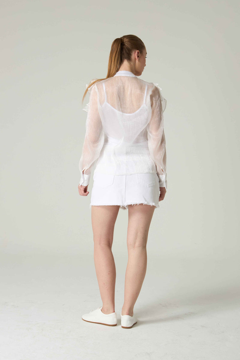 Person wearing a white outfit with sheer sleeves on a plain background.